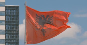 Albanian flag waving against a modern city backdrop, symbolizing national pride.