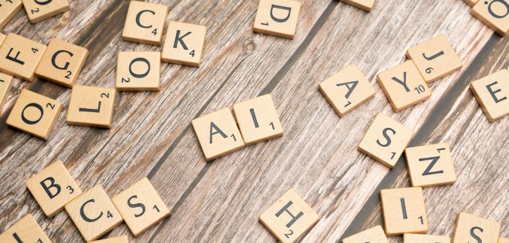 Wooden letter tiles scattered on a textured surface, spelling 'AI'.