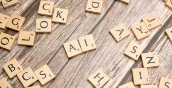 Wooden letter tiles scattered on a textured surface, spelling 'AI'.