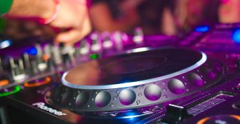 Close-up of a DJ's hands on mixing console at a vibrant party in Utrecht.