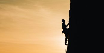 A silhouette of a rock climber scaling a steep cliff during sunset in Russia, showcasing determination and adventure.