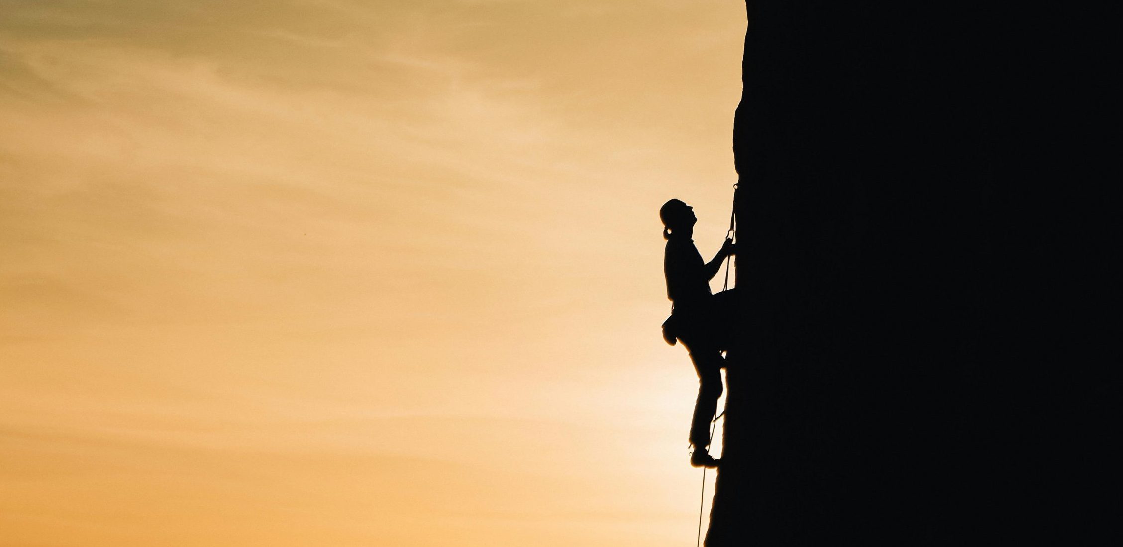 A silhouette of a rock climber scaling a steep cliff during sunset in Russia, showcasing determination and adventure.
