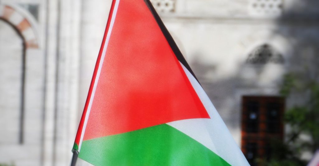 Palestinian flag waving outside historic building, symbolizing cultural pride.