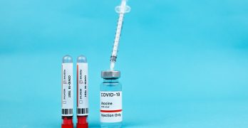 Vaccine vial and blood test tubes labeled COVID-19 on a blue surface, representing healthcare progress.