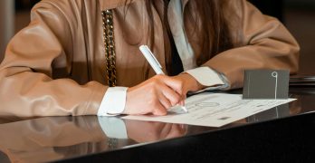 Close-up of a woman signing a document at a sleek reception counter, indoor setting.