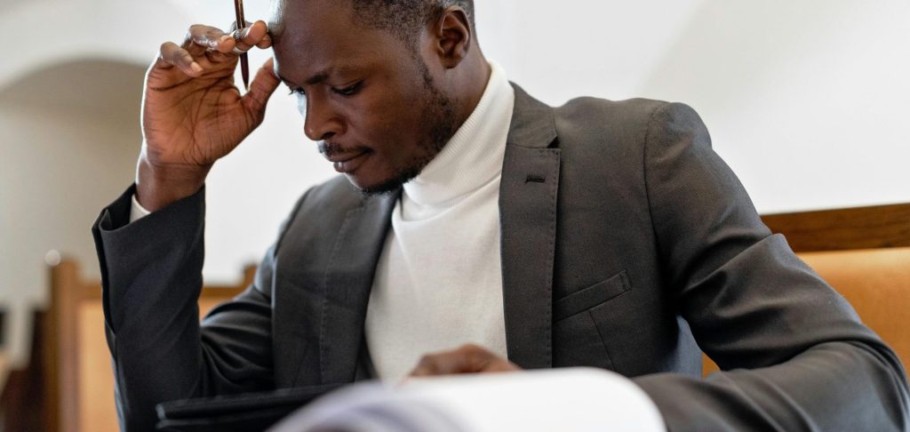 A focused businessman in a suit examines documents while deep in thought in an office setting.