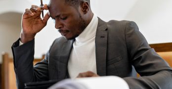 A focused businessman in a suit examines documents while deep in thought in an office setting.
