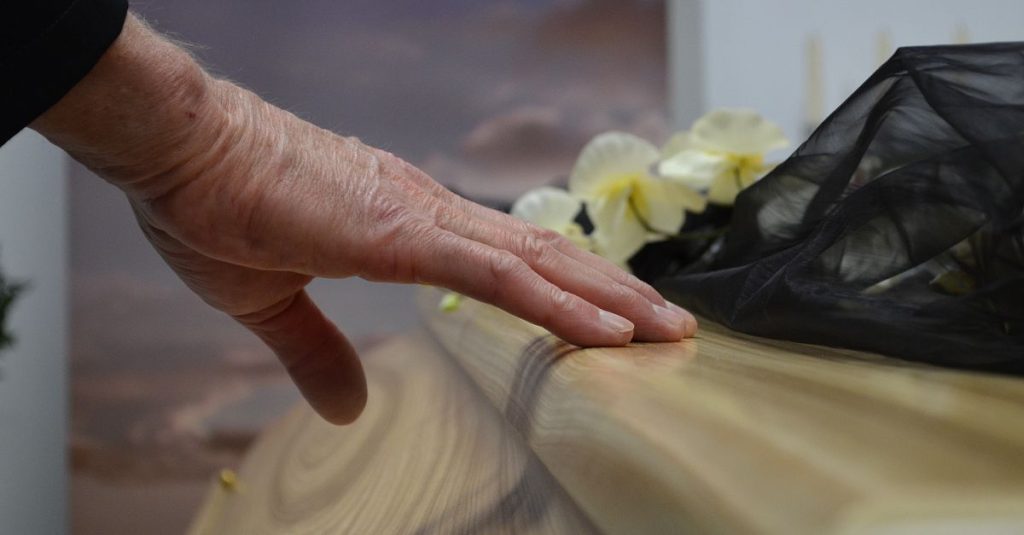 A touching moment of grief as a hand rests on a coffin, symbolizing loss and mourning.