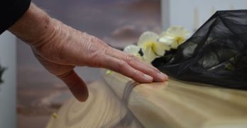A touching moment of grief as a hand rests on a coffin, symbolizing loss and mourning.