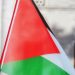 Palestinian flag waving outside historic building, symbolizing cultural pride.