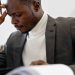 A focused businessman in a suit examines documents while deep in thought in an office setting.